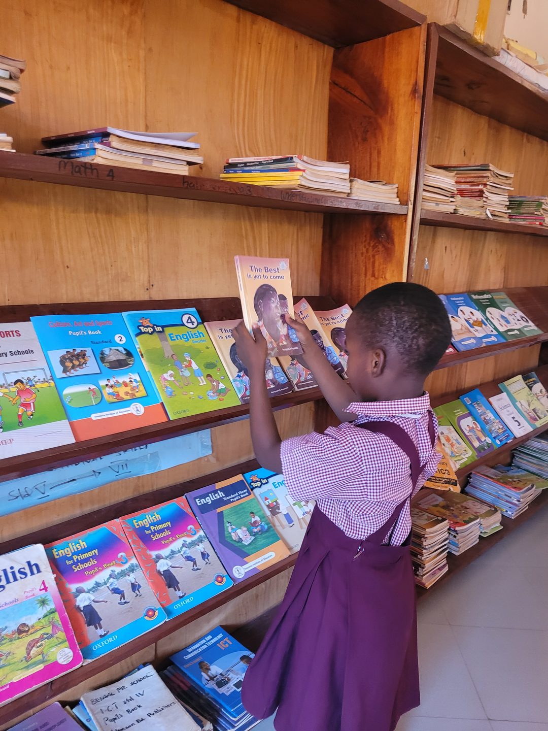 A young pupil reaching up to choose a book from the school bookshelves