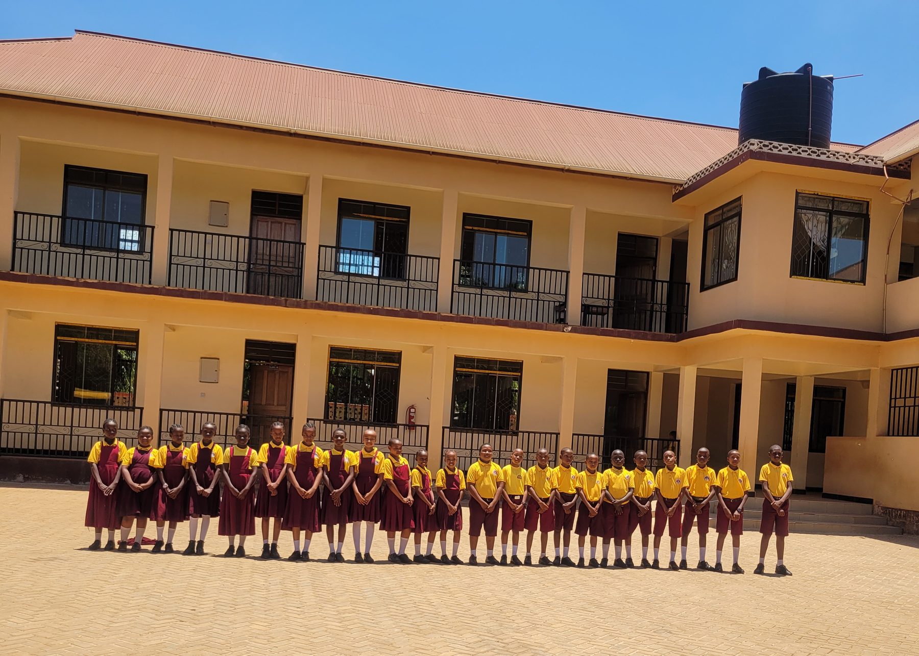 A row of Bensal pupils in uniform standing in front of the two-storey classroom block